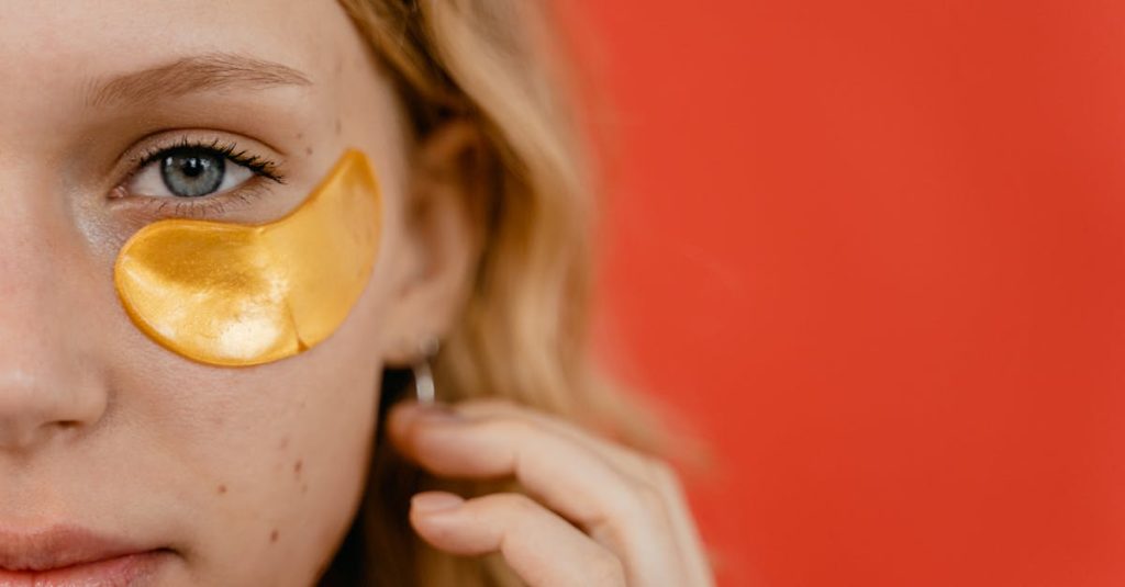 Close-up of a young woman with a gold eye patch against a vibrant red background, highlighting skincare routine.